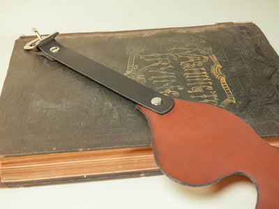 Bound by Dave Leather Blindfold with black strap and metal buckle resting on a vintage book