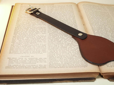 Leather Blindfold by Bound by Dave in brown leather with buckle strap on open book background