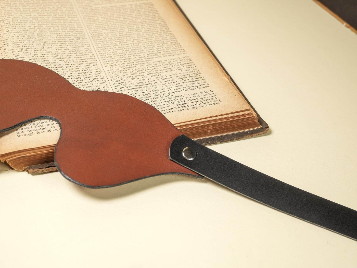 Leather Blindfold by Bound by Dave with brown front and black adjustable strap on a cream surface