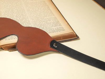 Leather Blindfold by Bound by Dave with brown front and black adjustable strap on a cream surface