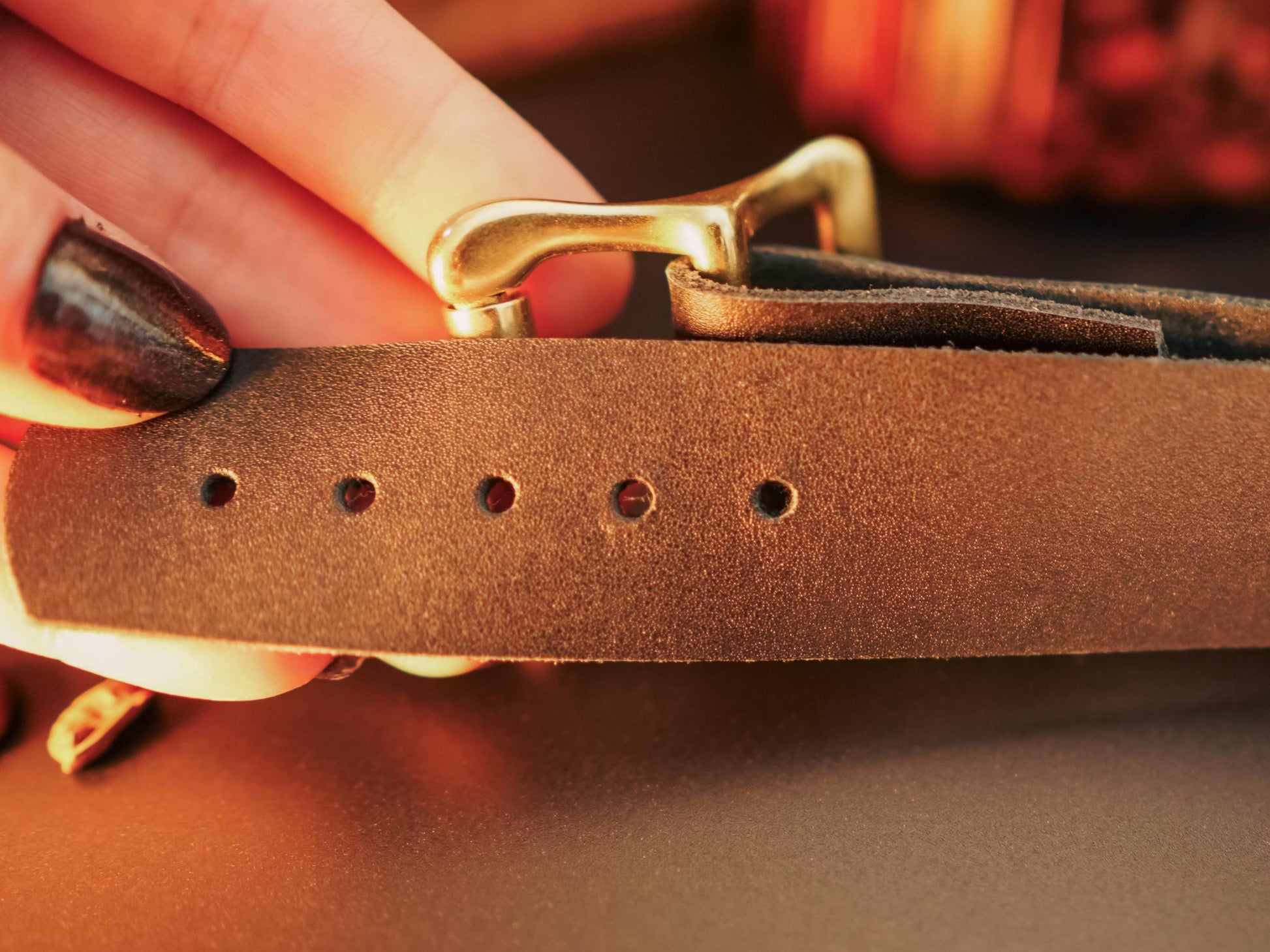 Close up of brown leather hand cuffs with metal buckle held by a hand with dark nail polish
