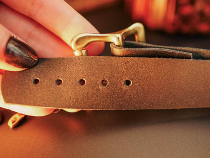 Close up of brown leather hand cuffs with metal buckle held by a hand with dark nail polish