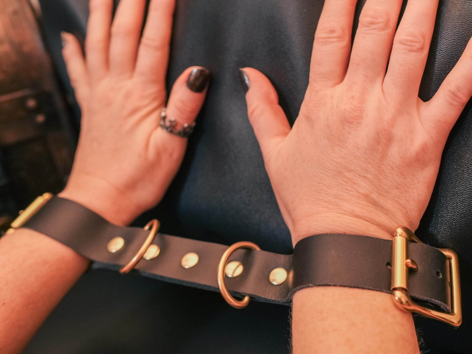 Leather Hand Cuffs from Bound by Dave securing wrists with brass hardware on black leather straps