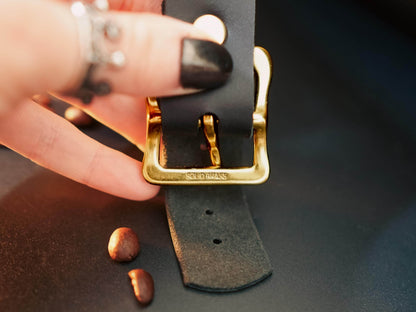 Black leather hand cuffs with solid brass buckle held by hand with dark nail polish