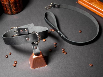 Bound by Dave black locking collar with metal buckle and attached copper bell on gray surface