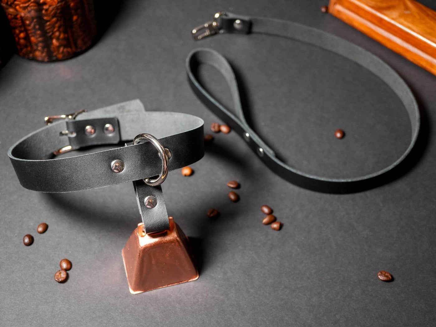 Bound by Dave black locking collar with metal buckle and attached copper bell on gray surface