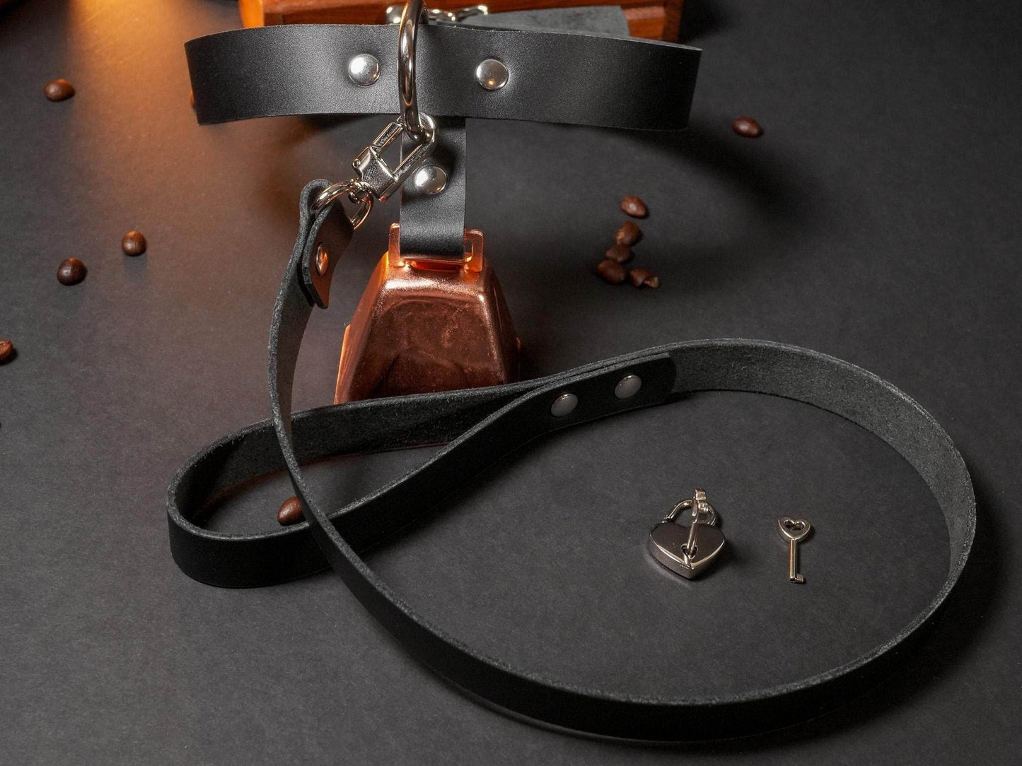 Black leather locking collar with attached leash and small padlock with key on black surface