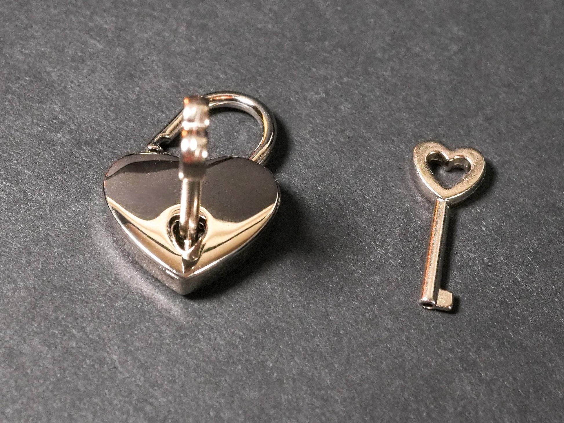 Bound by Dave heart-shaped silver lock with matching key locking collar accessory on gray background
