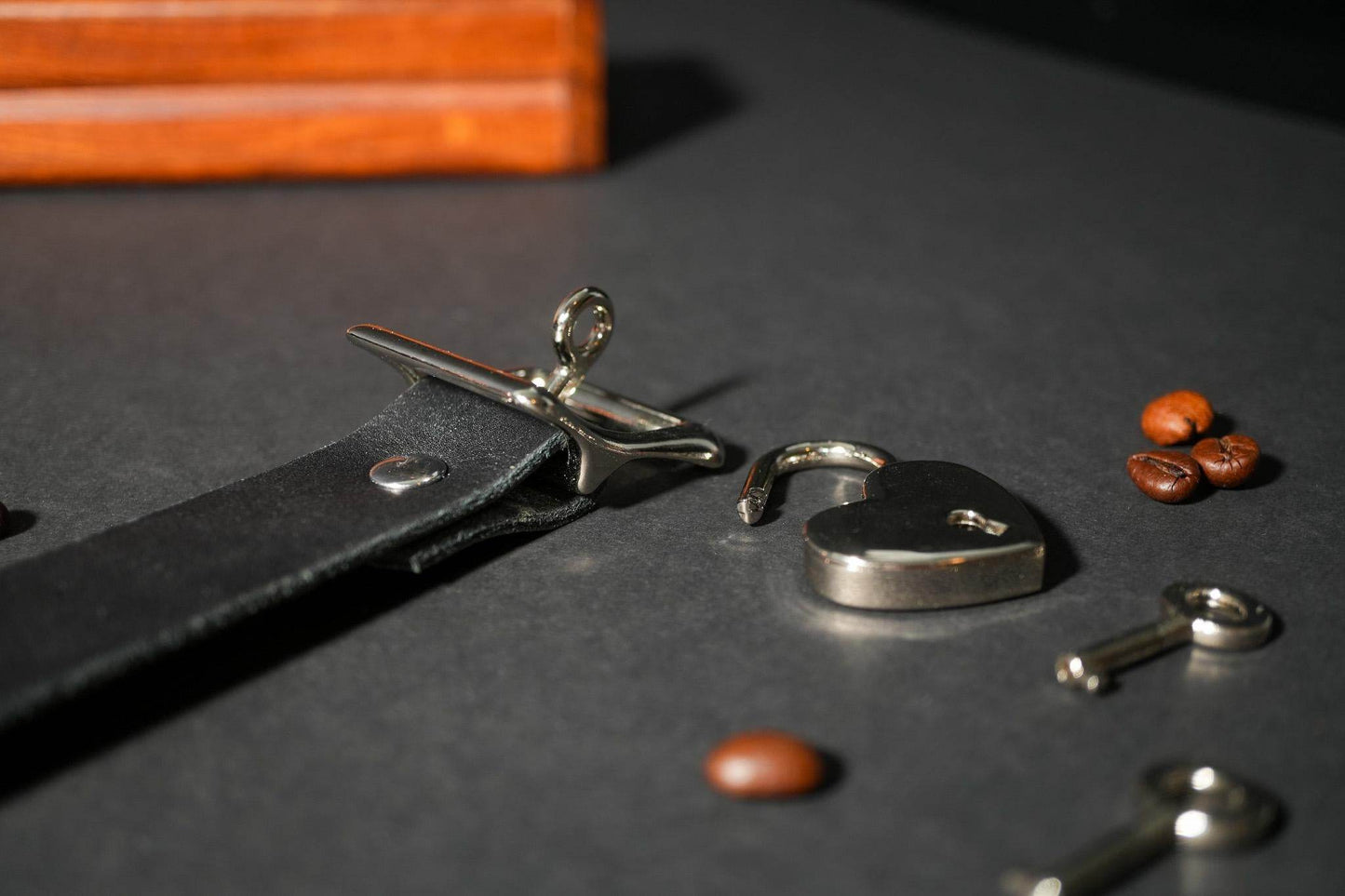 Bound by Dave black leather locking collar with silver heart-shaped padlock and key on dark surface