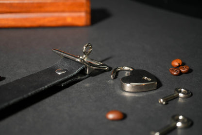 Bound by Dave black leather locking collar with silver heart-shaped padlock and key on dark surface