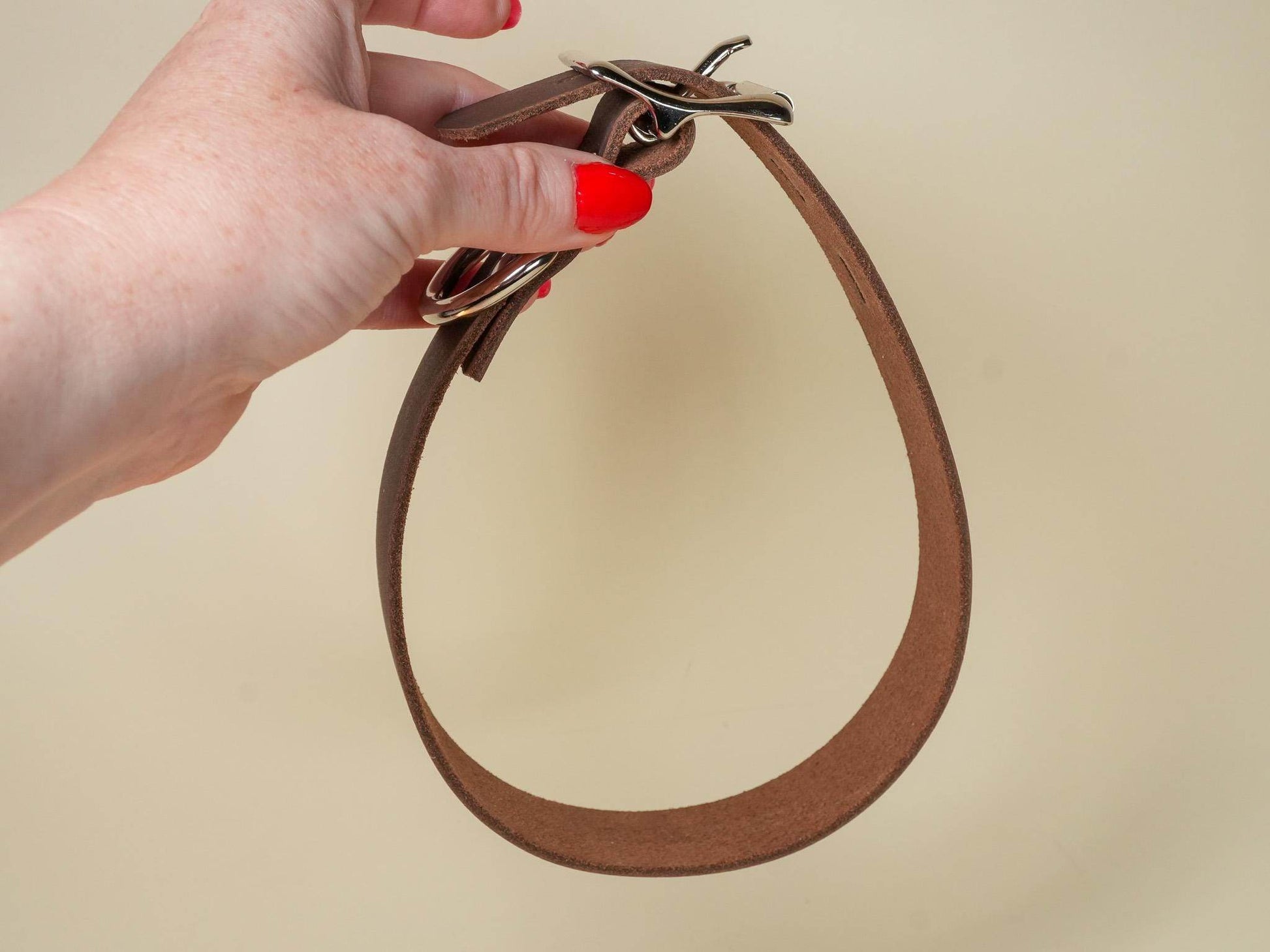 Hand holding a brown leather Locking Sub Collar with metal buckle and ring by Bound by Dave