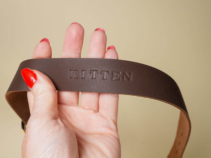 Brown leather Locking Sub Collar embossed with the word KITTEN held in hand by Bound by Dave