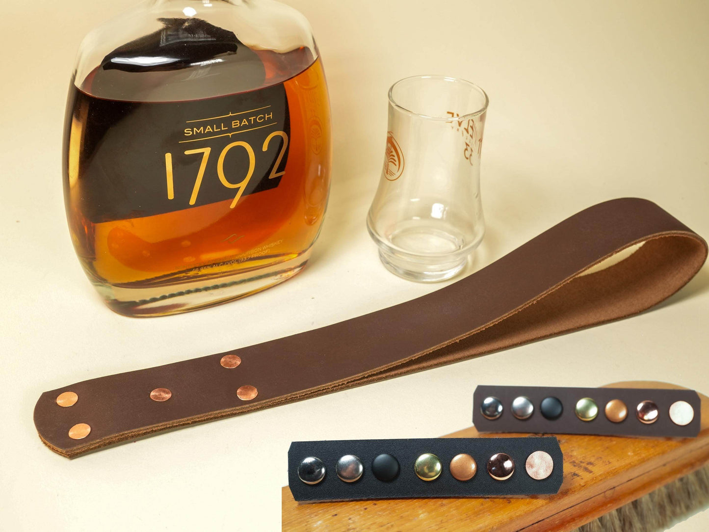 Bound by Dave leather spanking belt with metal studs displayed next to a whiskey bottle and glass