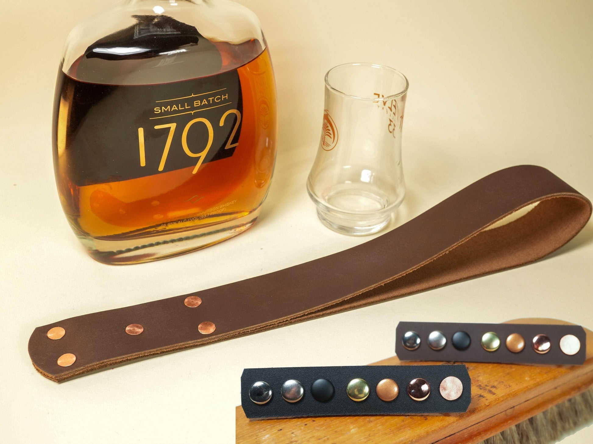 Bound by Dave leather spanking belt with metal studs displayed next to a whiskey bottle and glass