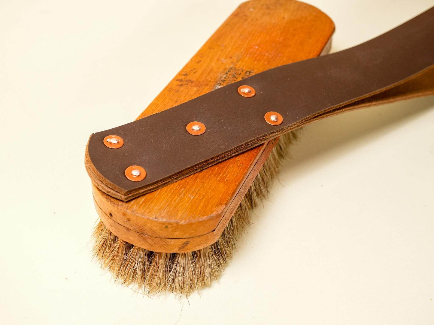 Leather spanking belt with copper rivets laid over wooden hairbrush with natural bristles