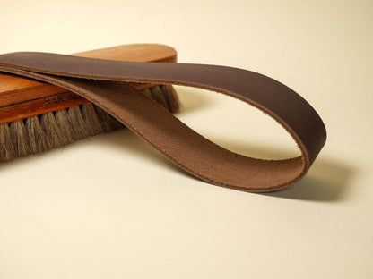 Brown leather spanking belt by Bound by Dave displayed on a wooden brush on light background