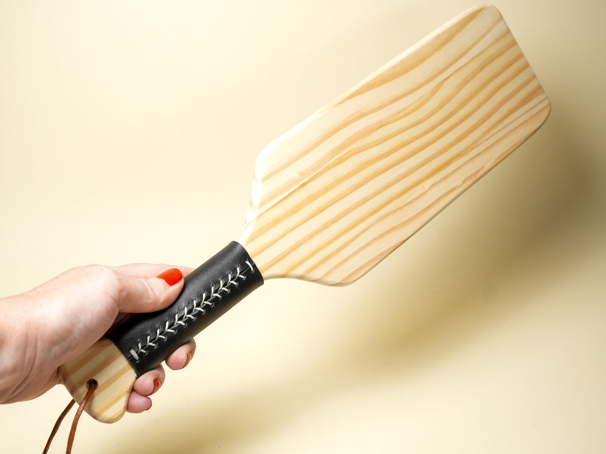 Wooden Spanking Paddle with black leather handle held in hand by Bound by Dave