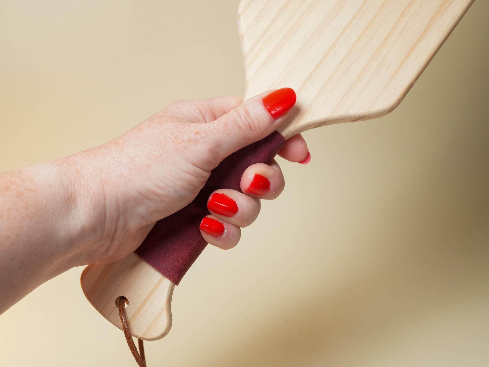 Hand holding a wooden Spanking Paddle with polished surface and leather-wrapped handle by Bound by Dave