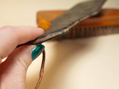 Close-up of a hand holding a leather paddle showing the edge and leather paddle holes
