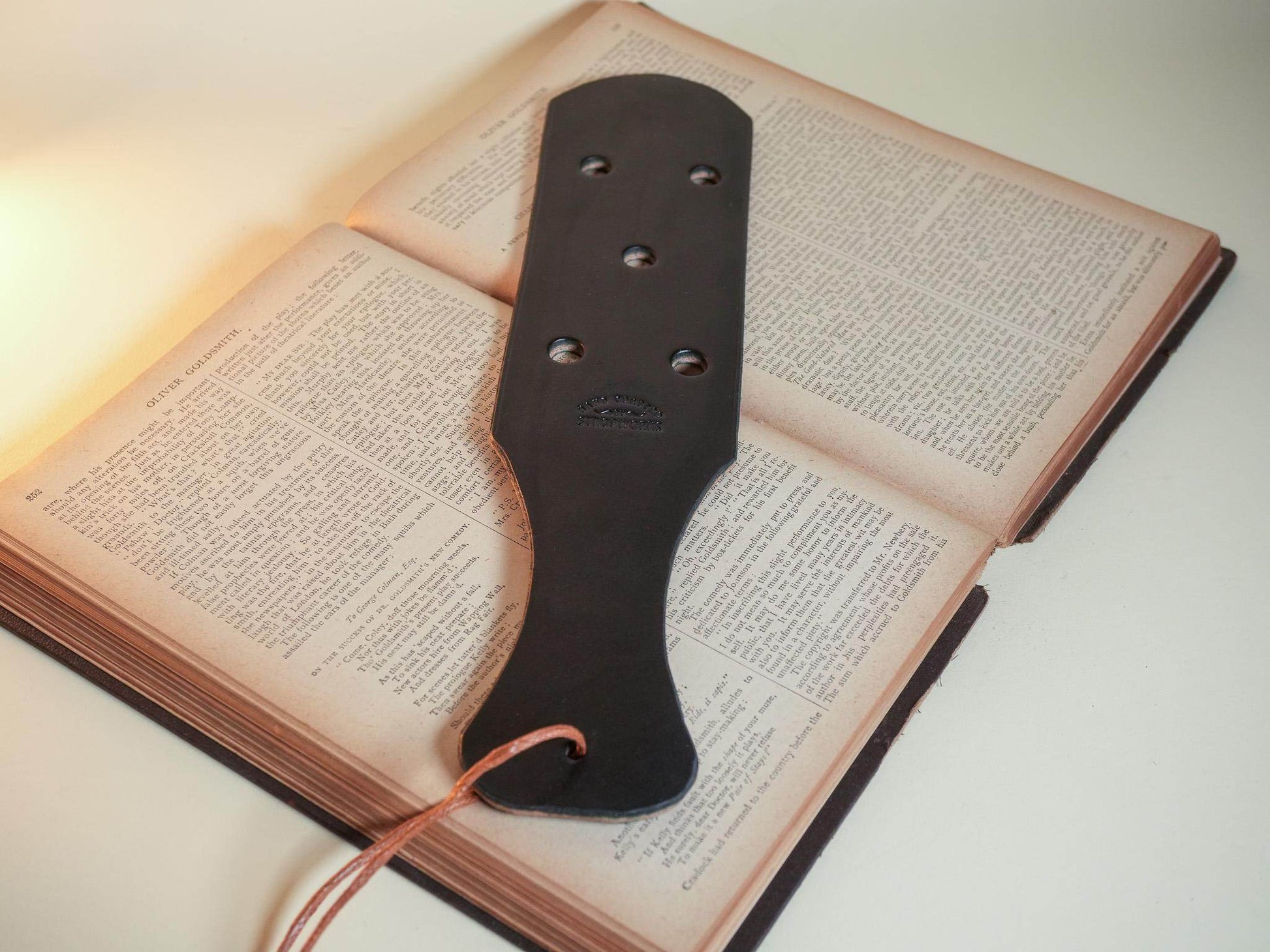 Bound by Dave black leather paddle with six Leather Paddle Holes resting on an open book