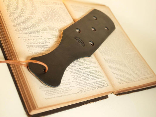 Bound by Dave black leather paddle with holes lying open on a vintage book