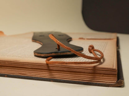 Leather Paddle Holes with brown leather strap resting on an open book with aged pages