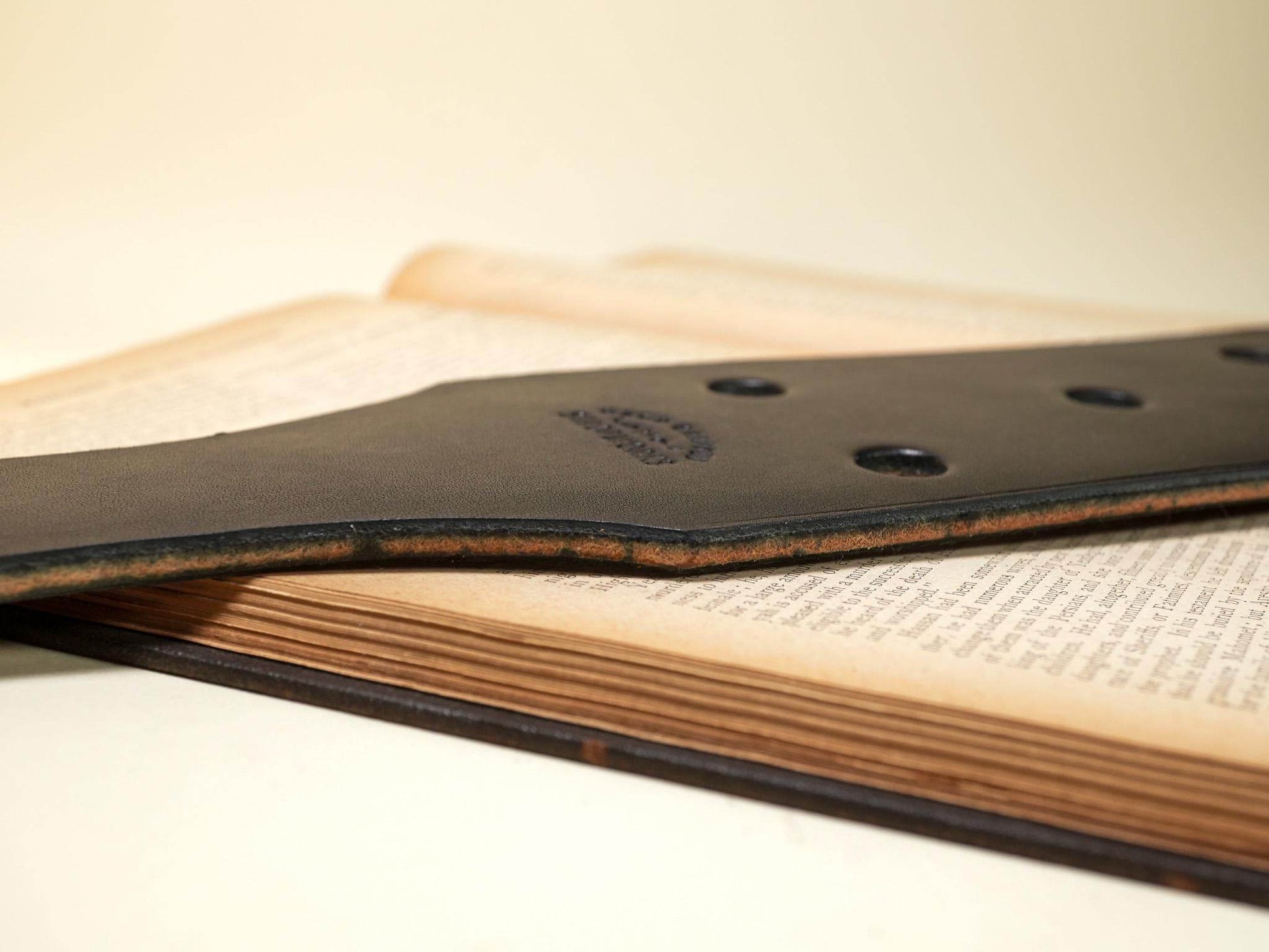 Close-up of Bound by Dave leather paddle with multiple Leather Paddle Holes on wooden surface