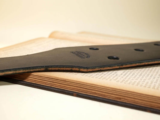 Close-up of Bound by Dave leather paddle with multiple Leather Paddle Holes on wooden surface