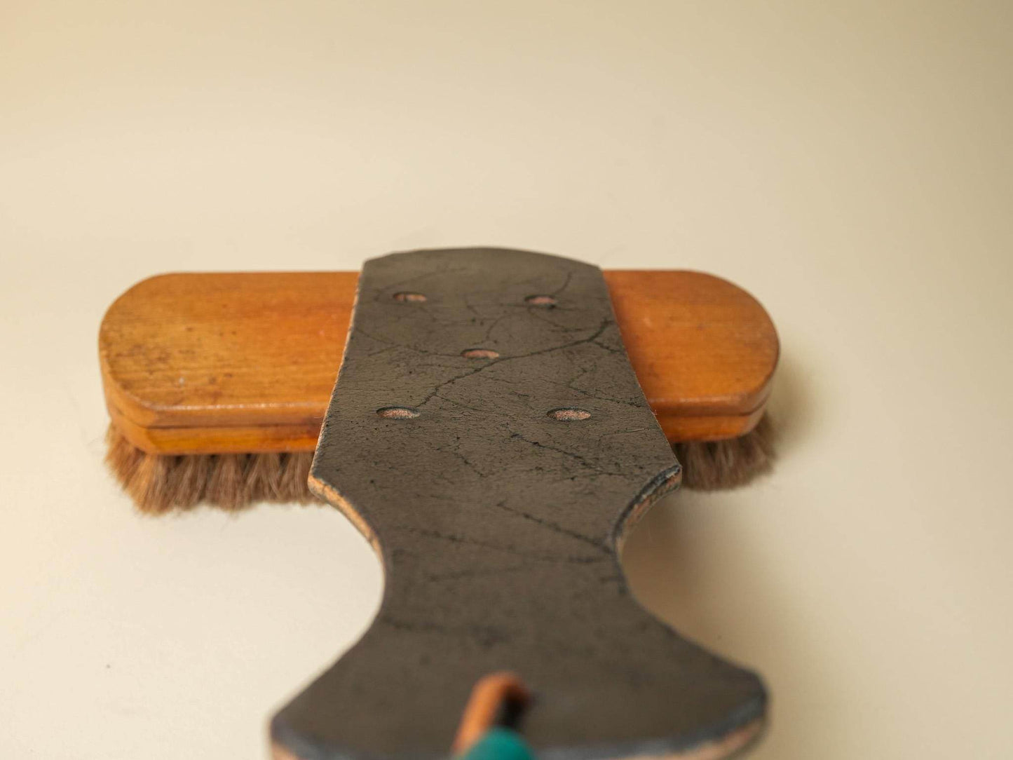 Leather paddle with multiple leather paddle holes resting on a wooden brush with natural bristles