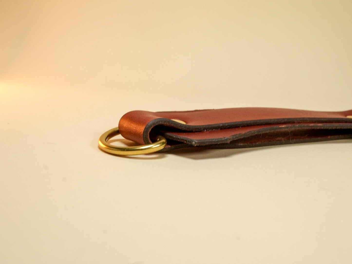 Bound by Dave brown leather Tawse with brass ring detail on beige background