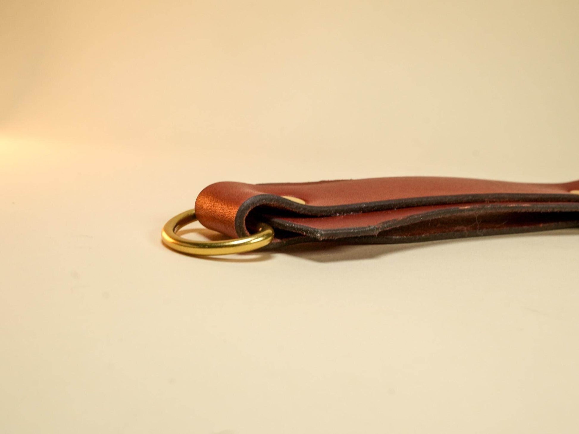 Bound by Dave brown leather Tawse with brass ring detail on beige background