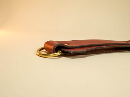 Bound by Dave brown leather Tawse with brass ring detail on beige background