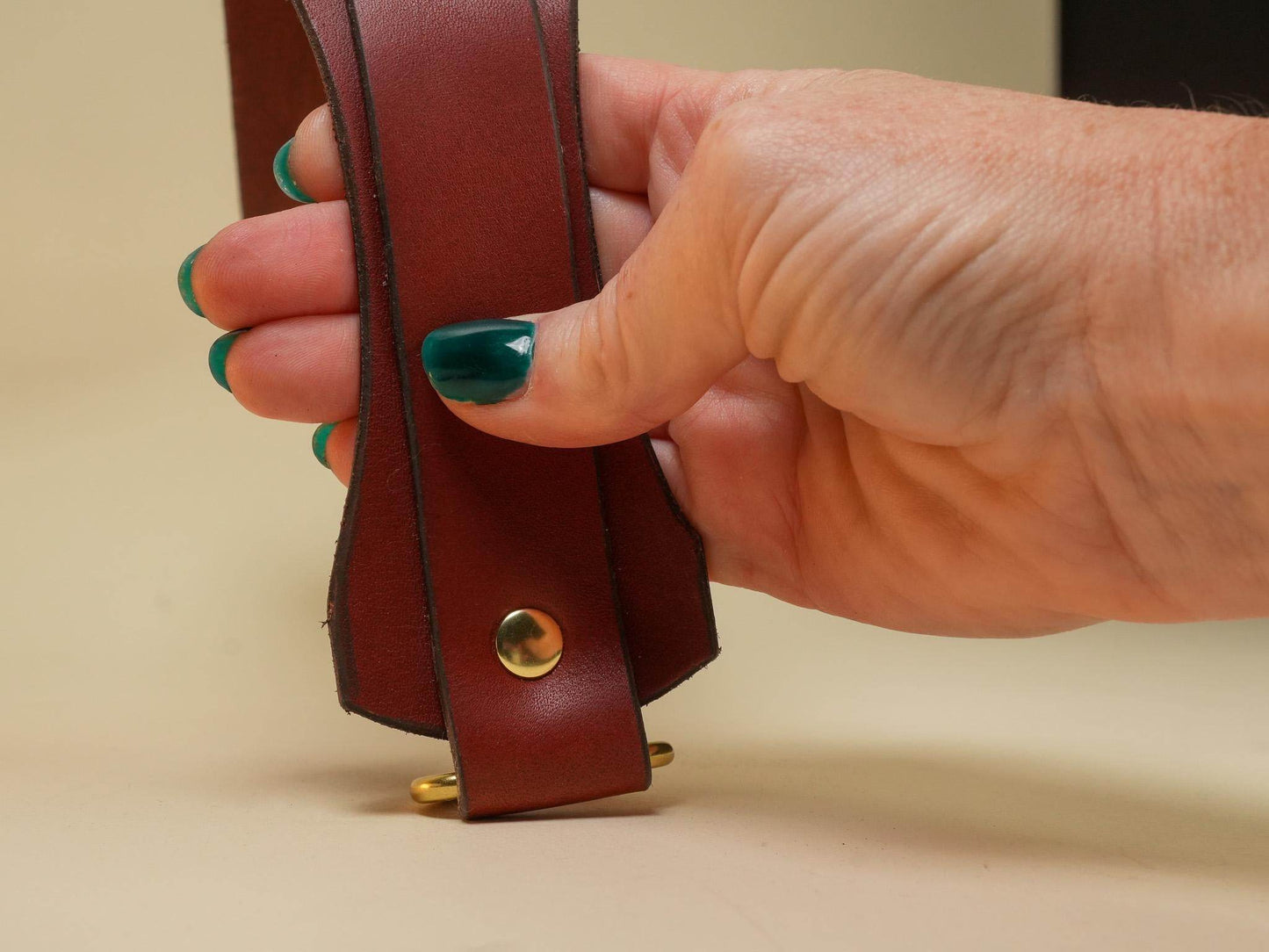 Hand holding a brown leather Tawse with brass rivets crafted by Bound by Dave