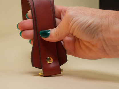 Hand holding a brown leather Tawse with brass rivets crafted by Bound by Dave