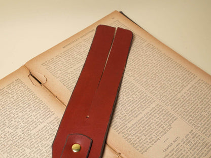 Bound by Dave brown leather Tawse paddle with brass rivet on vintage book pages
