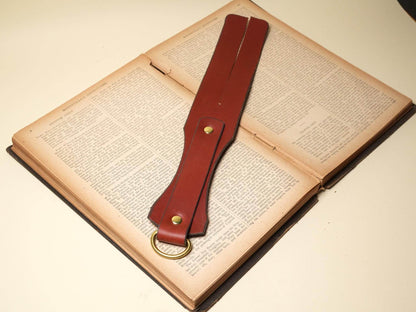 Bound by Dave brown leather Tawse with double straps and brass ring on an open book