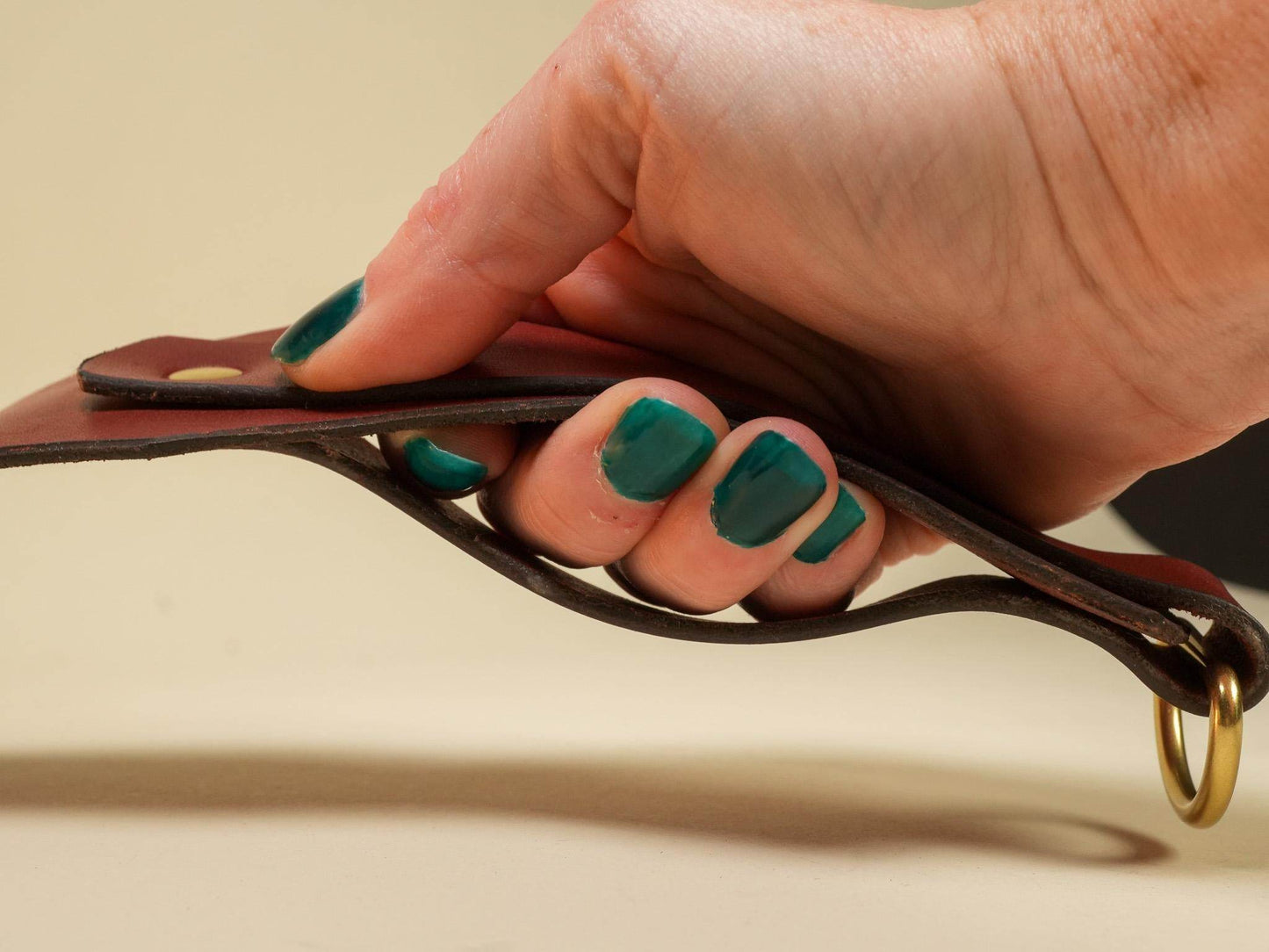 Hand holding a brown leather Tawse with metal ring, showing its flexible construction and handmade quality