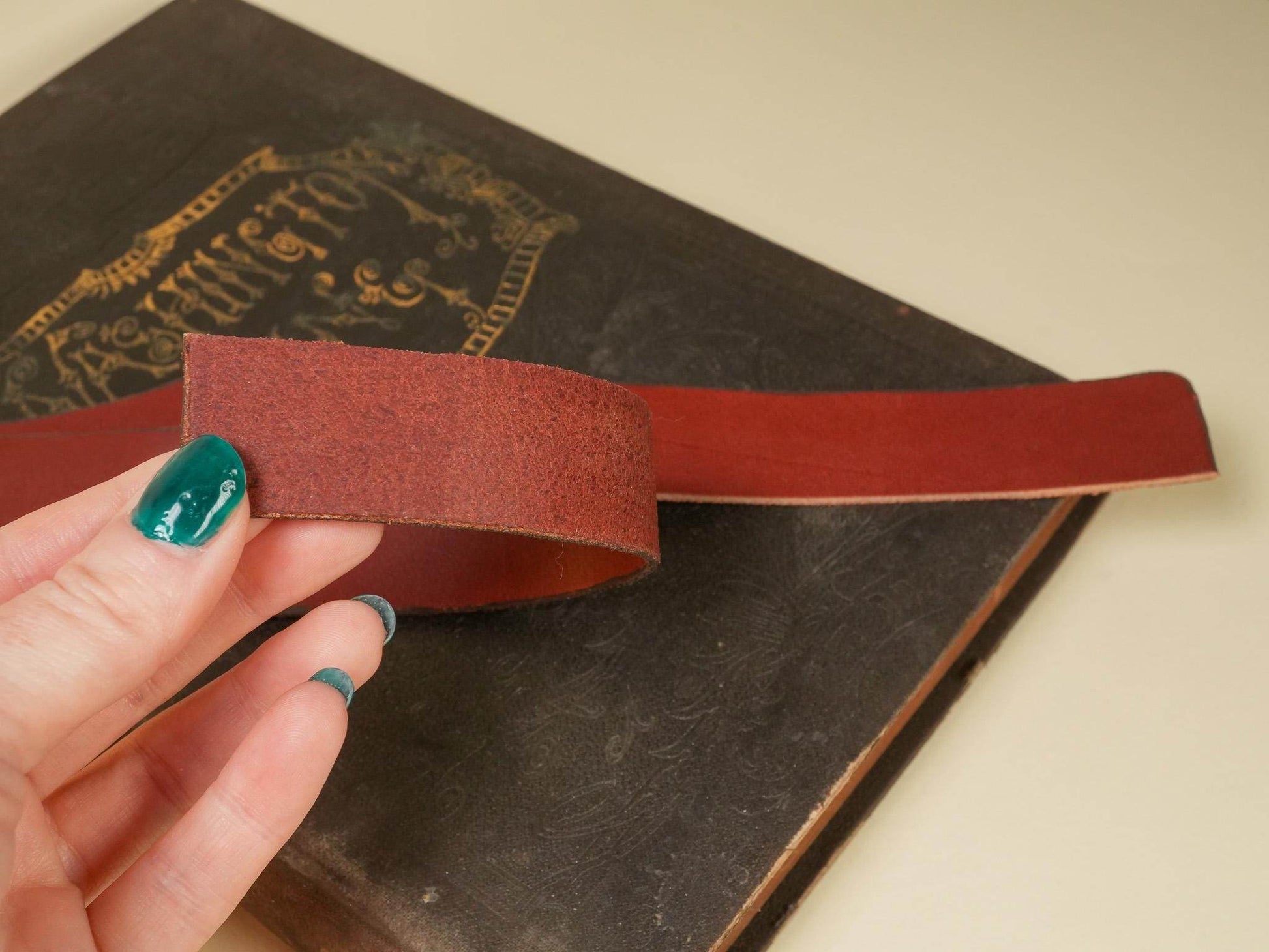 Brown leather Tawse held by hand with green nail polish above an old book background