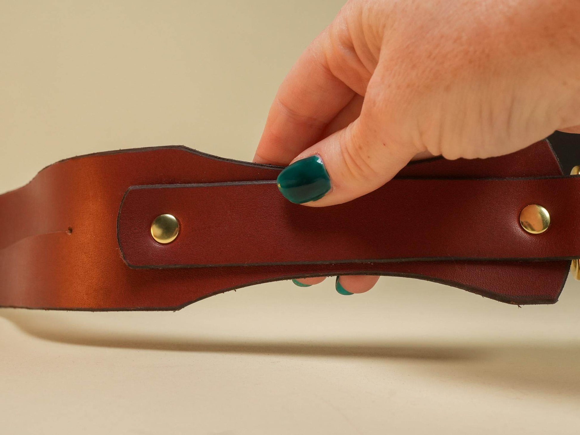 Hand holding a brown leather Tawse with brass rivets from Bound by Dave