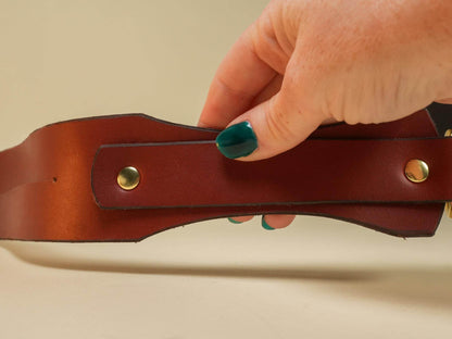 Hand holding a brown leather Tawse with brass rivets from Bound by Dave