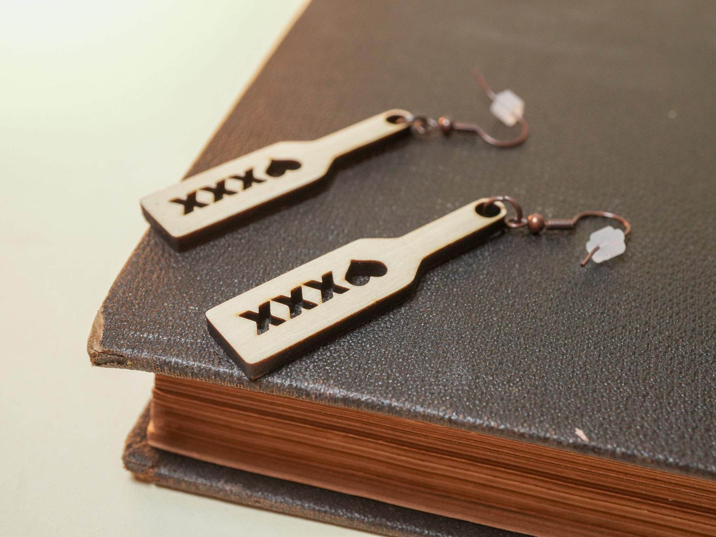 Bound by Dave wood spanking paddle earrings with heart and XXX cutout design on black book background