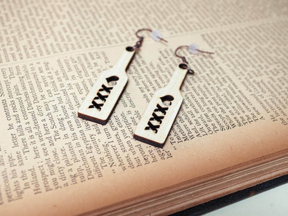 Bound by Dave wood spanking paddle earrings with heart and XXX cutouts on a book background