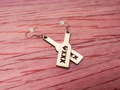 Bound by Dave wood spanking paddle earrings with triple X cutout design on a textured red surface