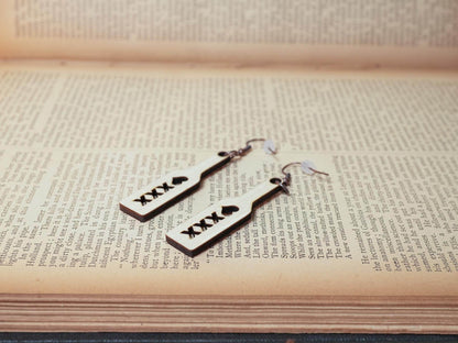Bound by Dave wood spanking paddle earrings with black XXX and heart symbols on book background