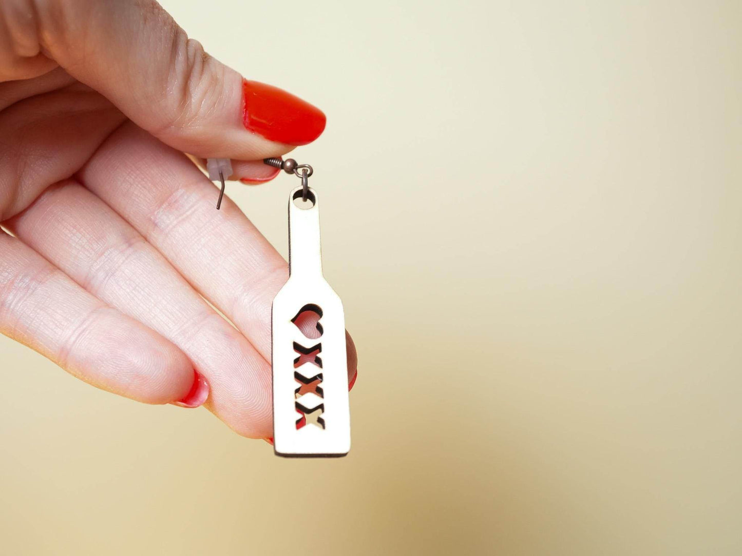 Hand holding a wood spanking paddle earrings with heart and XXX cut-out design